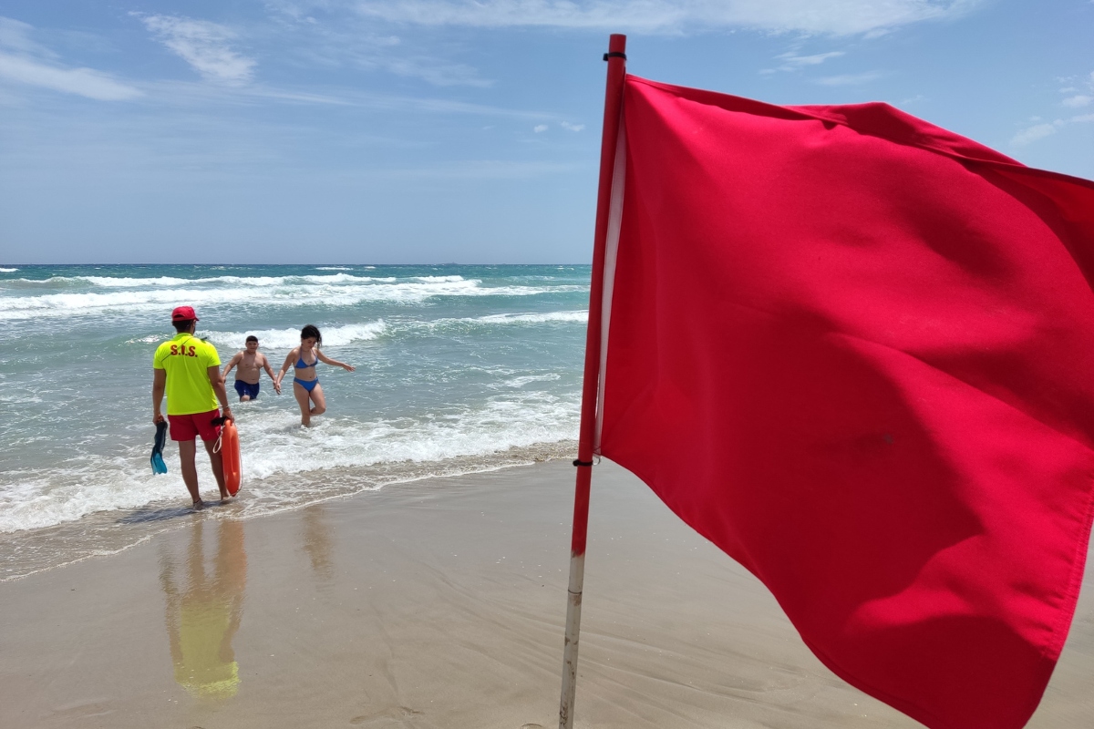	Imagen de archivo de un socorrista ordenando a unos bañistas que salgan del agua en una playa de La Manga con bandera roja.